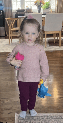 a little girl in a pink sweater is holding a pink cup