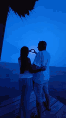 a man and woman are making a heart shape with their hands in front of the moon