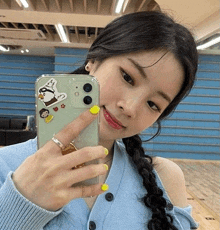 a woman is taking a selfie with her phone while wearing a blue cardigan and yellow nails .