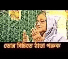 a woman with glasses is praying with her hands together in front of a curtain .