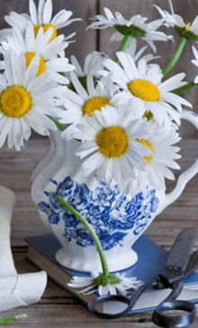 a blue and white pitcher filled with daisies sits on a book