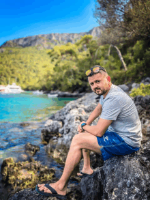 a man sits on a rock near the water wearing shorts that say m on them