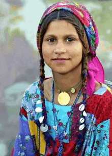 a young girl wearing a necklace and a head scarf looks at the camera