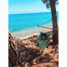 a person in a green shirt is laying in a hammock by the ocean