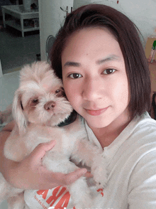 a woman holding a small white dog wearing a white shirt that says " asia "