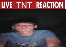 a boy in a blue shirt stands in front of a live tnt reaction sign