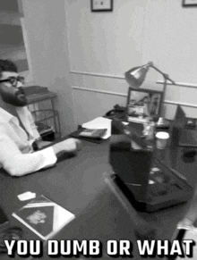 a black and white photo of a man sitting at a desk with the words you dumb or what above him