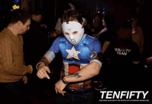 a man wearing a mask and a captain america shirt is dancing in front of a sign that says ten fifty