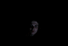 a man 's face is visible in the dark with his eyes closed