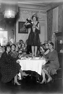 a woman is pouring a bottle of wine into a group of women sitting around a table