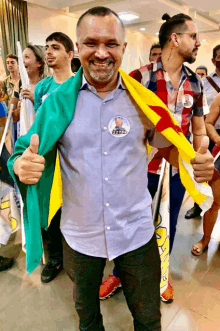 a man in a blue shirt with a sticker on his chest that says ' eptz ' gives a thumbs up