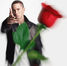 a man in a black jacket is holding a red rose and pointing at it