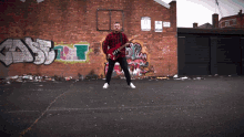 a man playing a guitar in front of a brick wall with graffiti on it that says ' a ' on it