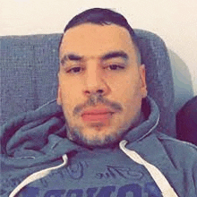 a man is sitting on a couch wearing a hoodie and taking a selfie .