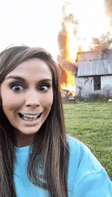 a woman in a blue sweatshirt is taking a selfie in front of a burning house .