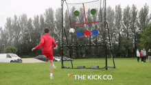 a boy in a red jacket is kicking a soccer ball in front of a goal that says the kick co. on it