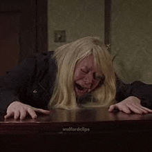 a woman is laying on a wooden table with her mouth open and her hands on the table .