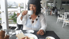 a woman sitting at a table drinking from a cup