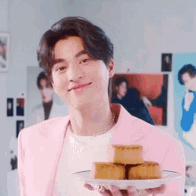 a young man in a pink jacket is holding a plate of cakes .