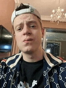 a young man wearing a hat and a gucci jacket is taking a selfie in a living room .