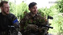 a man in a camouflage uniform is holding a gun next to another man in a camouflage uniform with the letters iv on it