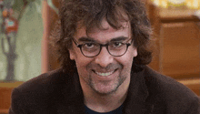 a man with curly hair and glasses is smiling