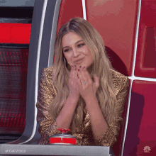 a woman in a gold sequined dress is sitting in a chair with a red button that says nbc on it