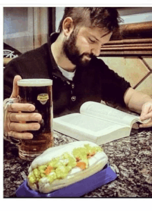 a man reading a book while holding a beer and a hot dog