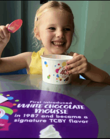 a little girl is sitting at a table with a cup of white chocolate mousse on it