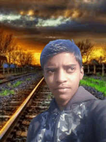 a young boy stands in front of a train track with a sunset in the background