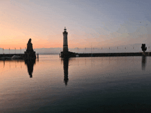 a lighthouse and a statue are reflected in the water