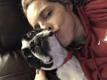 a woman in a red nike hoodie kisses a black and white dog on the nose