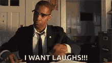 a man in a suit and tie is sitting at a desk and laughing while reading a book .