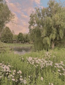 a lush green field with flowers and trees surrounding a body of water