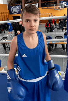 a young boy wearing blue adidas boxing gloves stands in a boxing ring