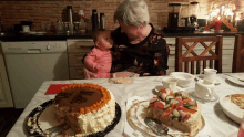 a woman holding a baby sits at a table with a cake that says marie on it