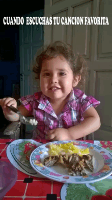 a little girl sitting at a table with a plate of food and the words cuando escuchas tu cancion favorita