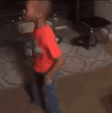 a young boy is standing in a living room wearing a red shirt and blue jeans .