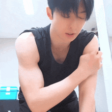 a young man in a black tank top holds his arm in pain