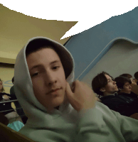 a young man wearing a white hoodie sits in a classroom