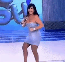 a woman in a blue dress is singing into a microphone while dancing on a stage .