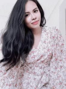 a woman with long black hair is wearing a white floral top