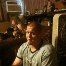 a man is sitting on a couch in a living room next to a fan and a dog .