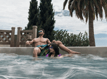 a man sits on the edge of a pool while a woman sits on his lap