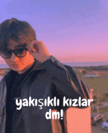 a young man wearing sunglasses and a black shirt with the words " yakisikli kizlar dm " written below him