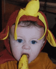 a baby wearing a red and yellow costume with a banana on his head eating a banana