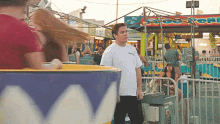 a man in a white shirt stands in front of a carnival ride with a sign that says ' a ' on it