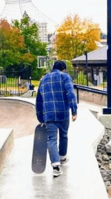 a man in a blue plaid shirt is carrying a skateboard down a ramp .