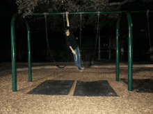 a person hanging upside down on a swing set in the dark