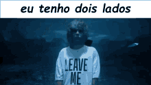 a man wearing a leave me shirt stands in the dark